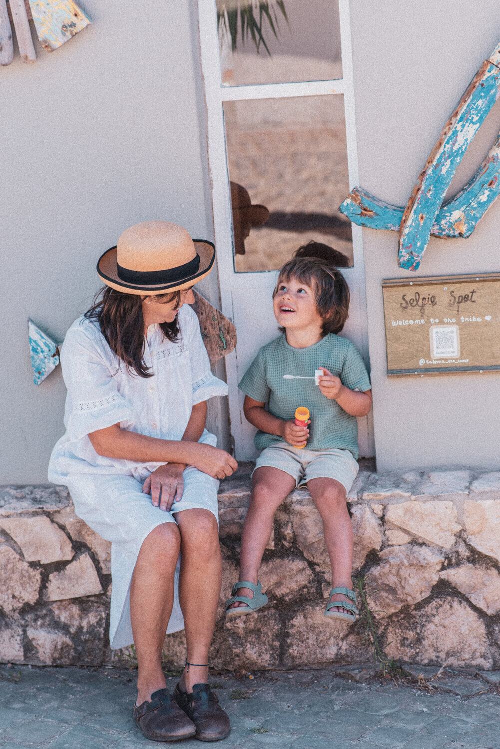 Mãe e filhos sentados a sorrir, com o filho a brincar com um brinquedo que faz bolas de sabão.