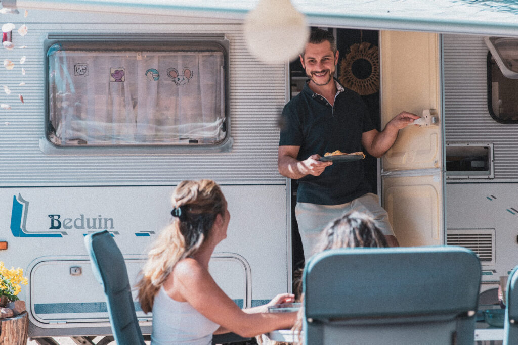 Homem sorrindo saindo de uma mobile home e mulher sentada em uma cadeira